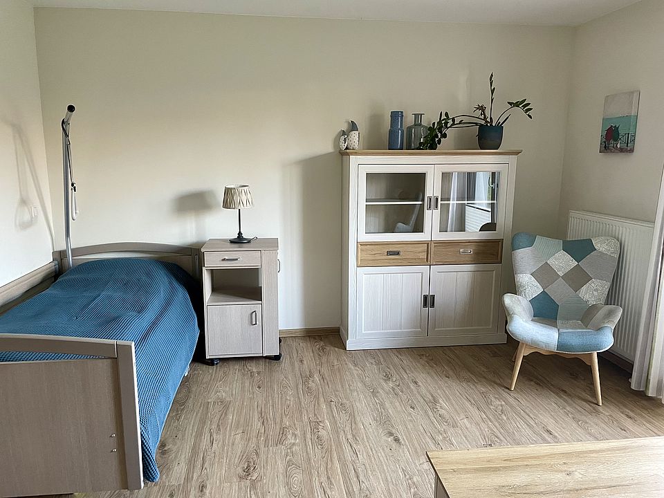 alt="Vollständig eingerichtetes Zimmer mit Bett, Tisch und Sitzgelegenheit"